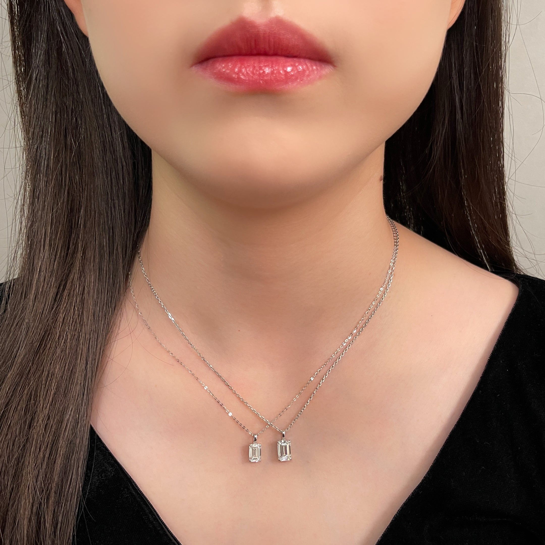 Model wearing two emerald-cut diamond pendants on chains for a pendant comparison