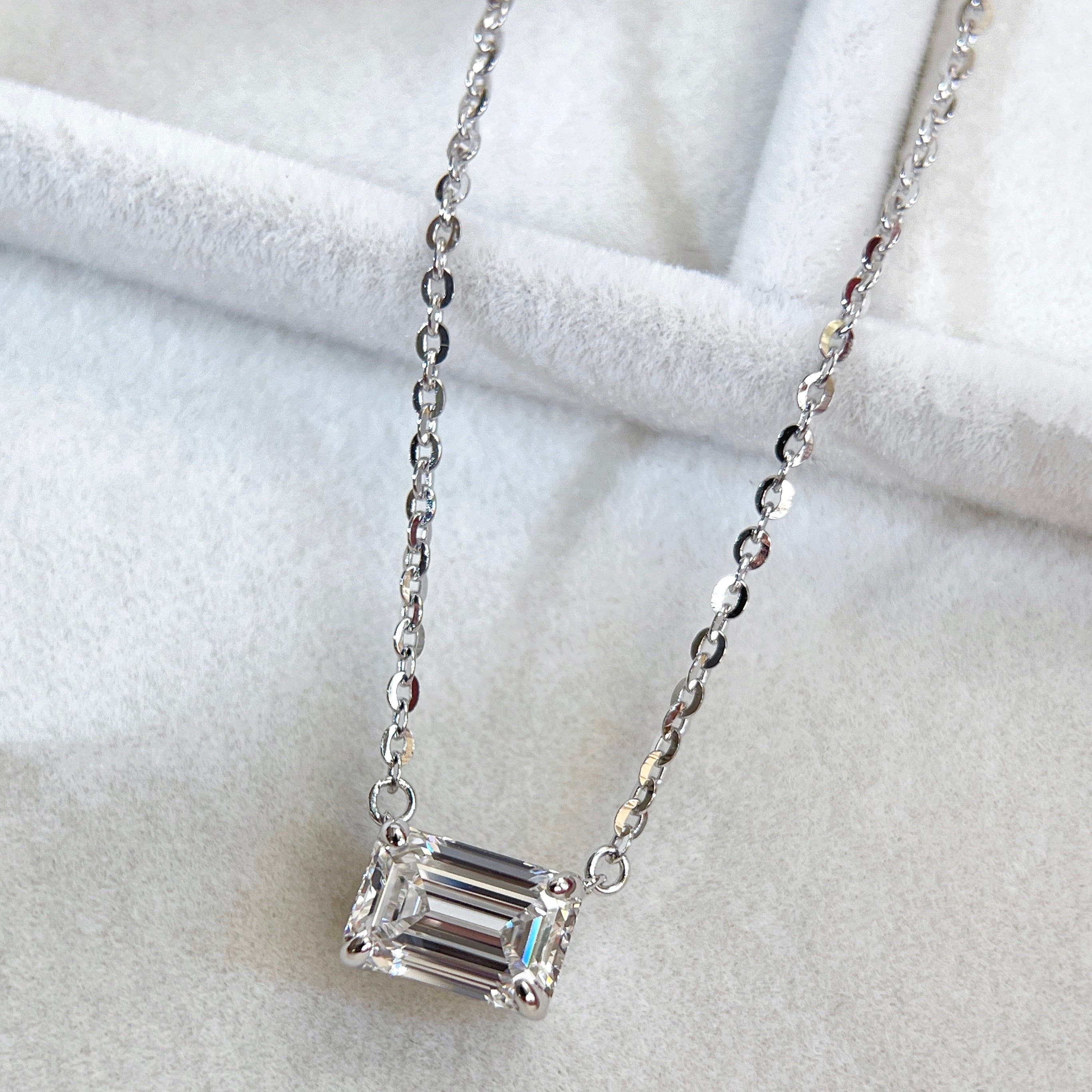 Angled display of an emerald-cut lab grown diamond in a four-prong sterling silver necklace setting