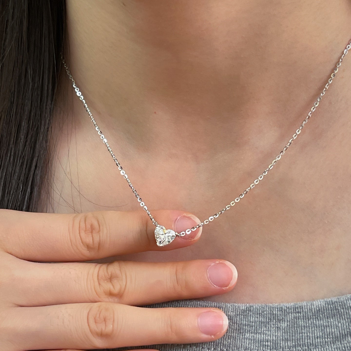 Model holding a 1.5 carat heart-shaped lab grown diamond necklace in S925 sterling silver.