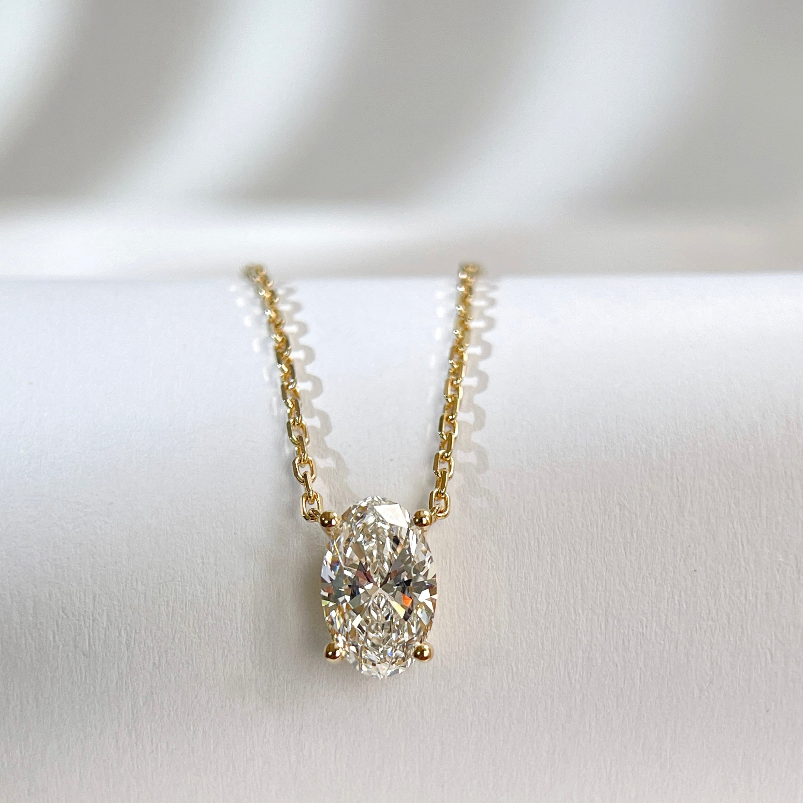 Front view of an oval lab-grown diamond four-prong necklace in yellow gold