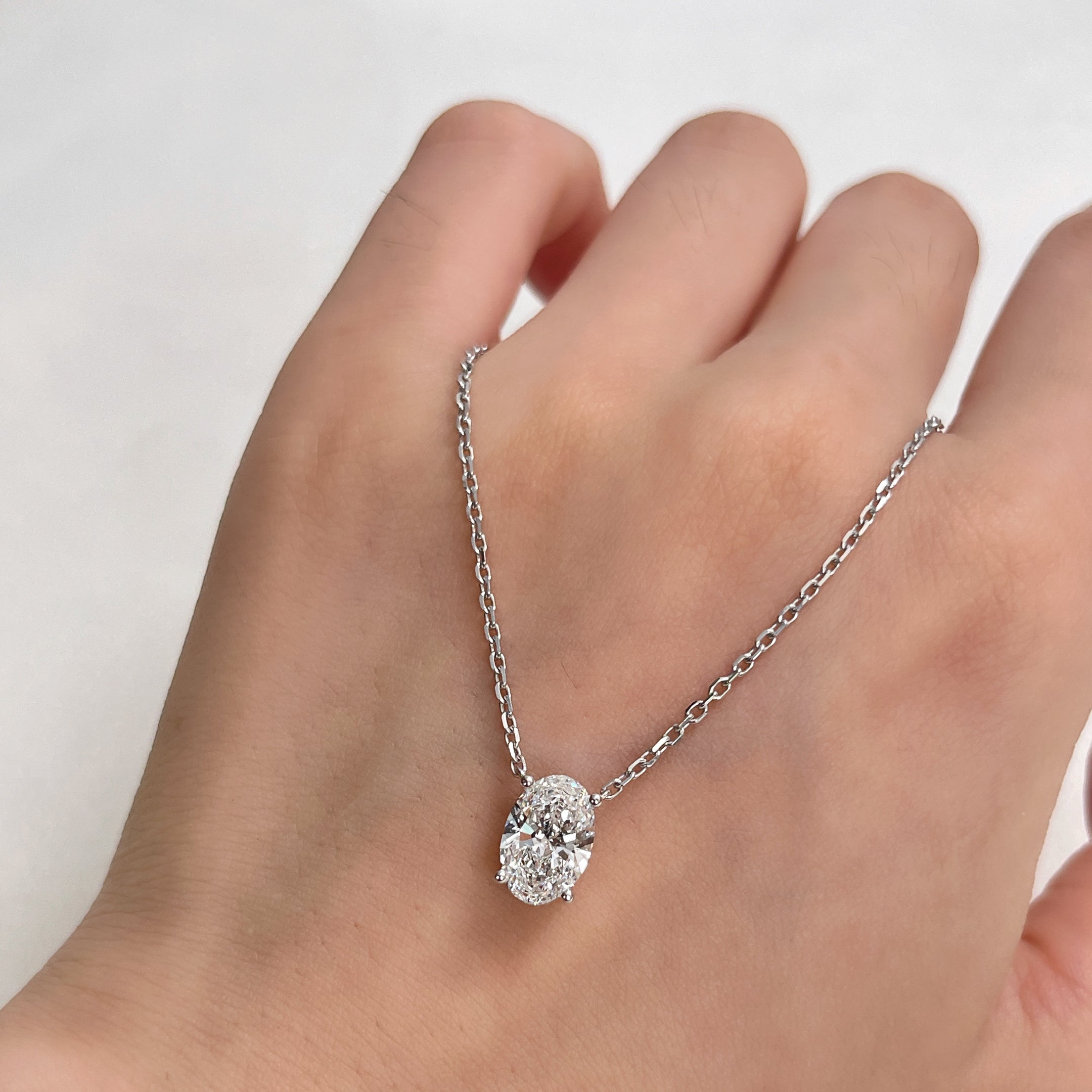 A 1.5 carat oval lab grown diamond necklace in S925 sterling silver displayed across a hand.