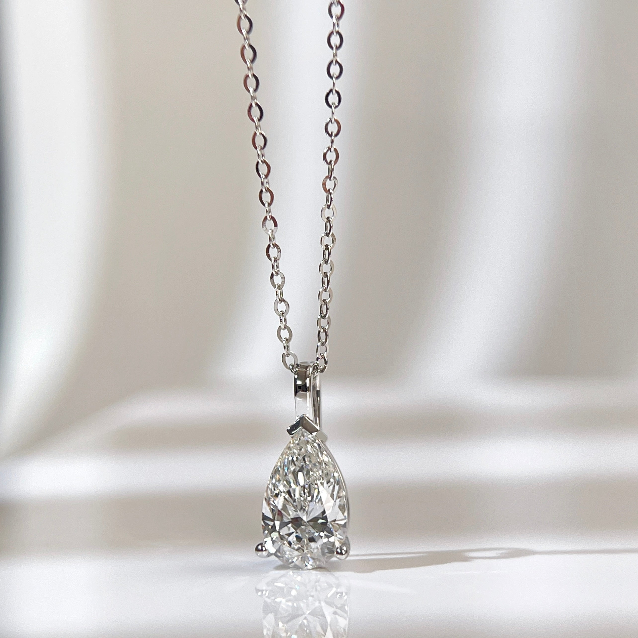 Front view of a 1.5 carat pear lab grown diamond pendant in 14K white gold styled on a chain; chain not included.