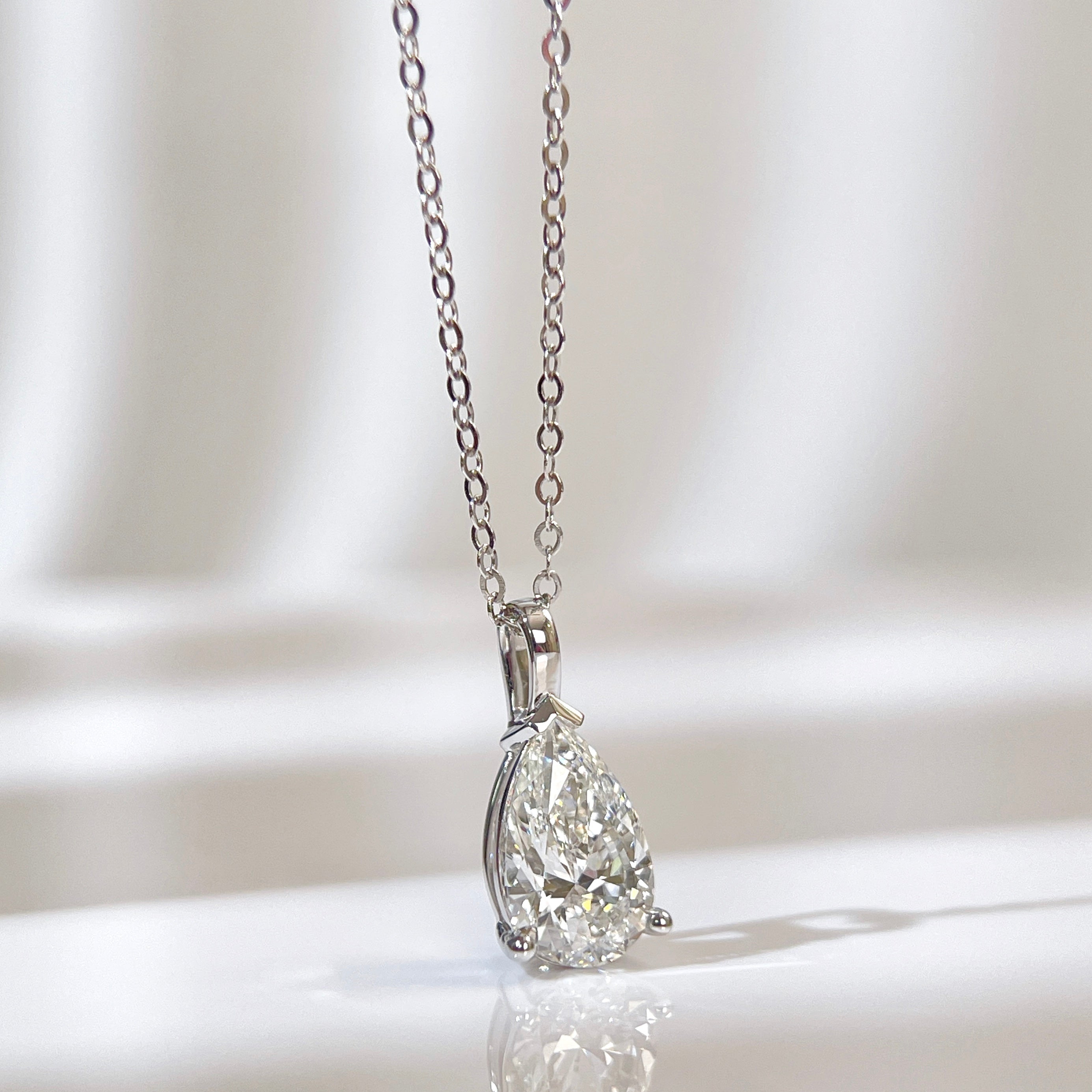 Front view of a 1.5 carat pear lab grown diamond pendant in 14K white gold styled on a chain; chain not included.