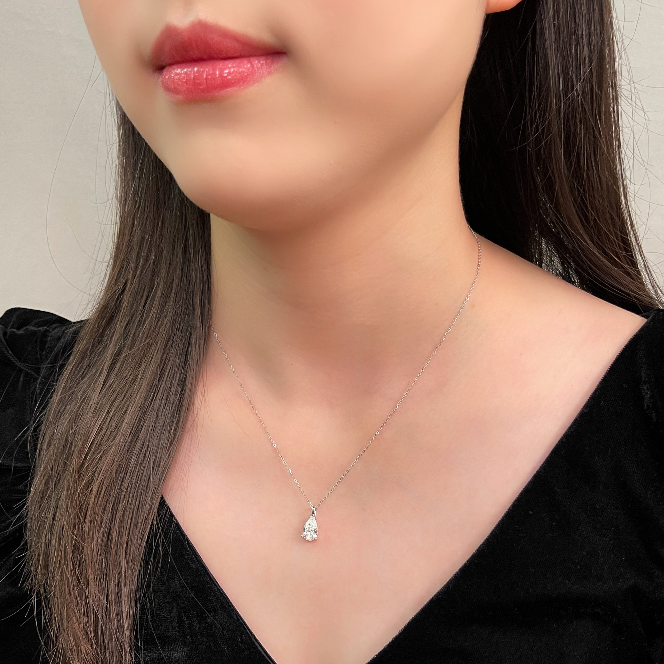 Side-profile view of a model wearing a 1.5 carat pear lab grown diamond pendant in 14K white gold styled on a chain; chain not included.