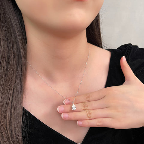 Model holding a 1.5 carat pear lab grown diamond pendant in 14K white gold styled on a chain; chain not included.