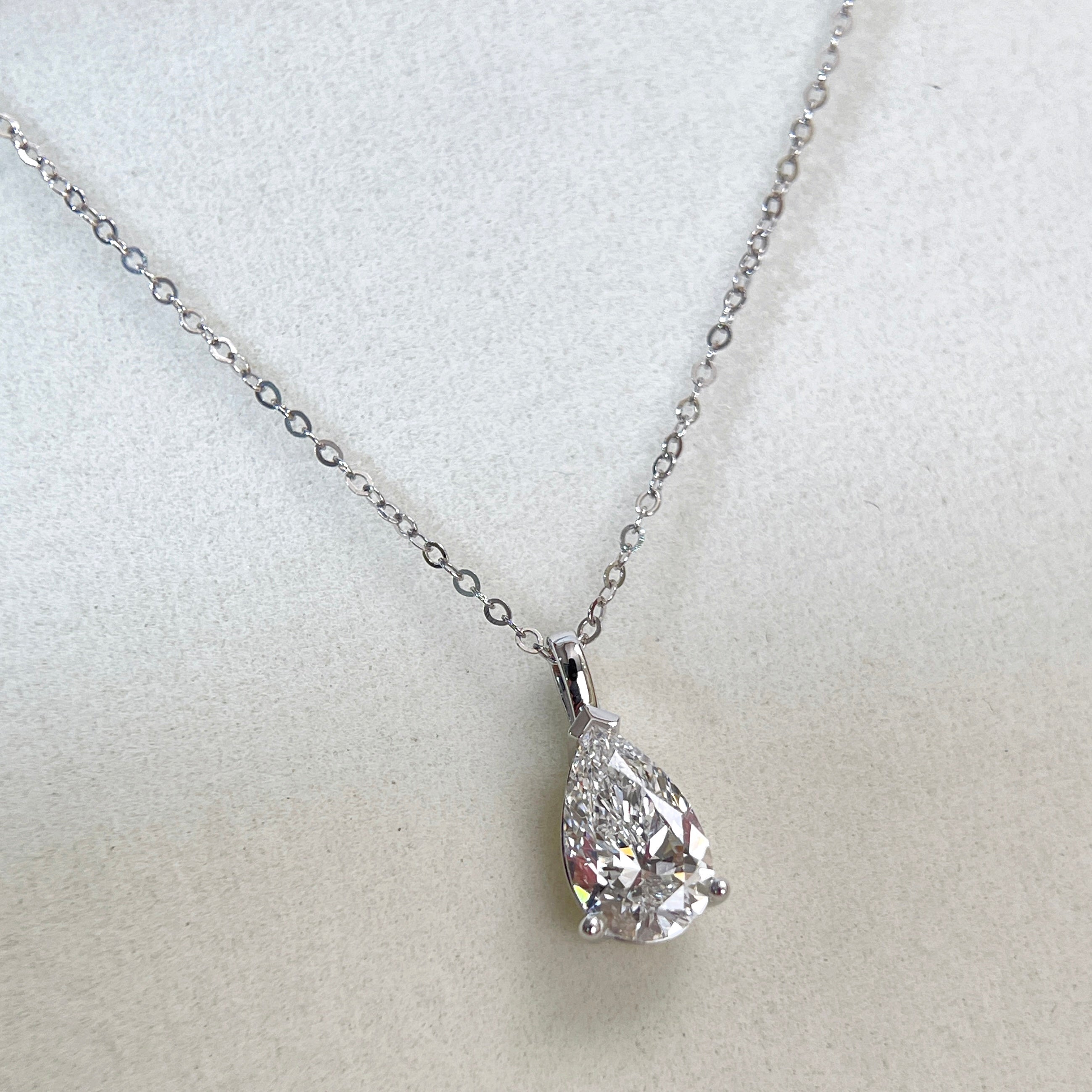 Angled view of a 1.5 carat pear lab grown diamond pendant in 14K white gold styled on a chain; chain not included.
