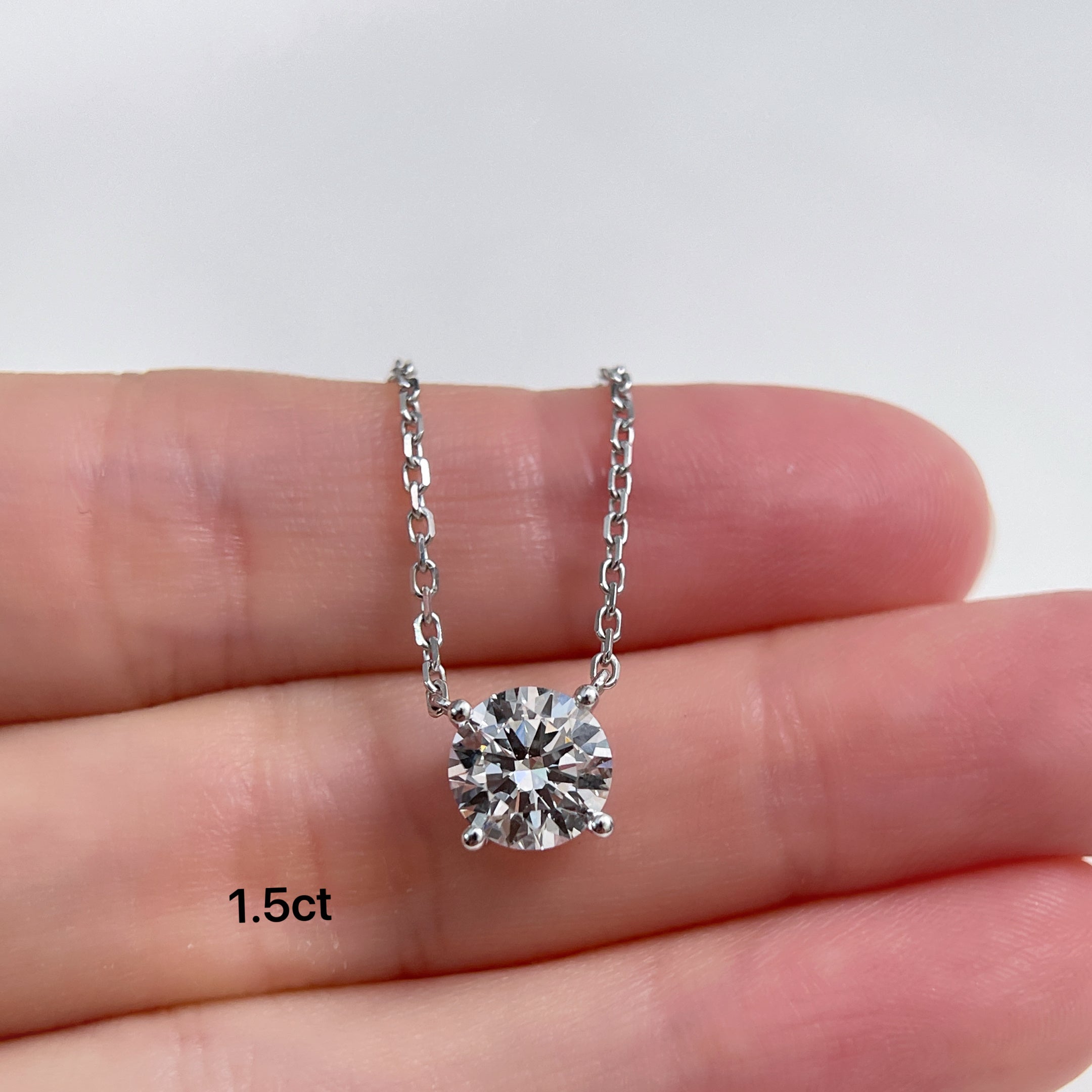 A 1.5 carat round lab grown diamond necklace displayed on a hand for scale.