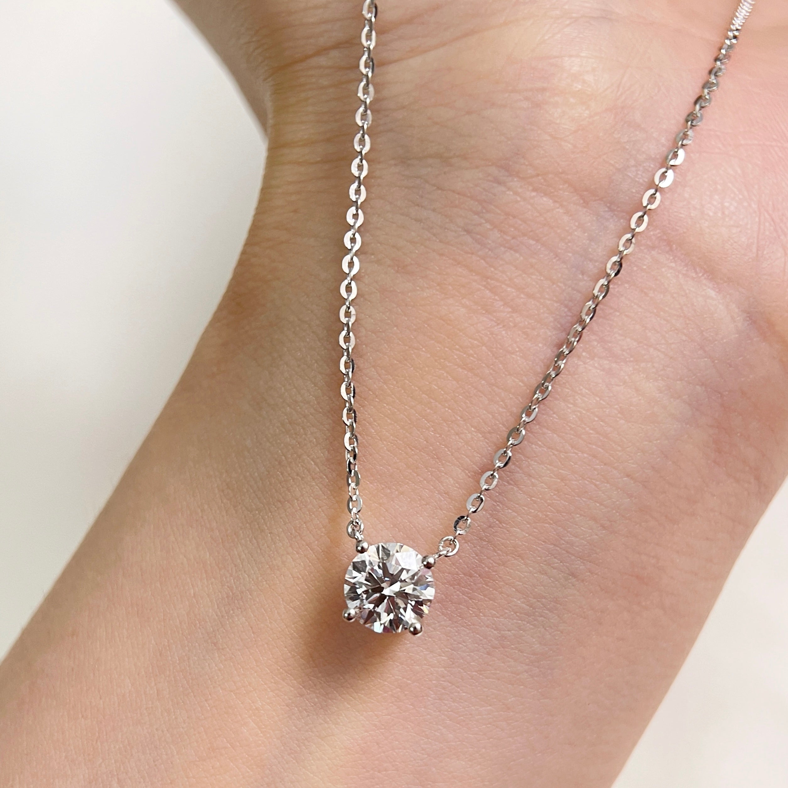 A 1.5 carat round lab grown diamond necklace in S925 sterling silver displayed on a hand.