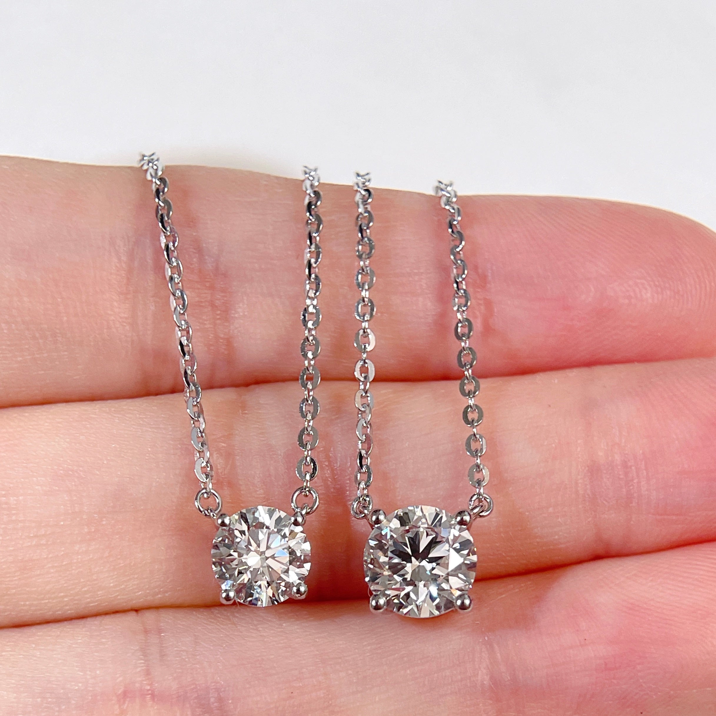 1 CT and 1.5 CT round lab grown diamond necklace size comparison displayed on a hand.