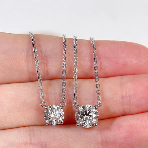 1 CT and 1.5 CT round lab grown diamond necklace size comparison displayed on a hand.