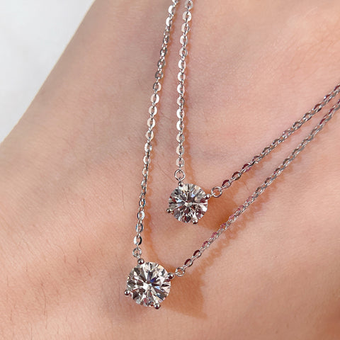 Full view of 1 CT and 1.5 CT round lab grown diamond necklaces displayed on a hand for size comparison.
