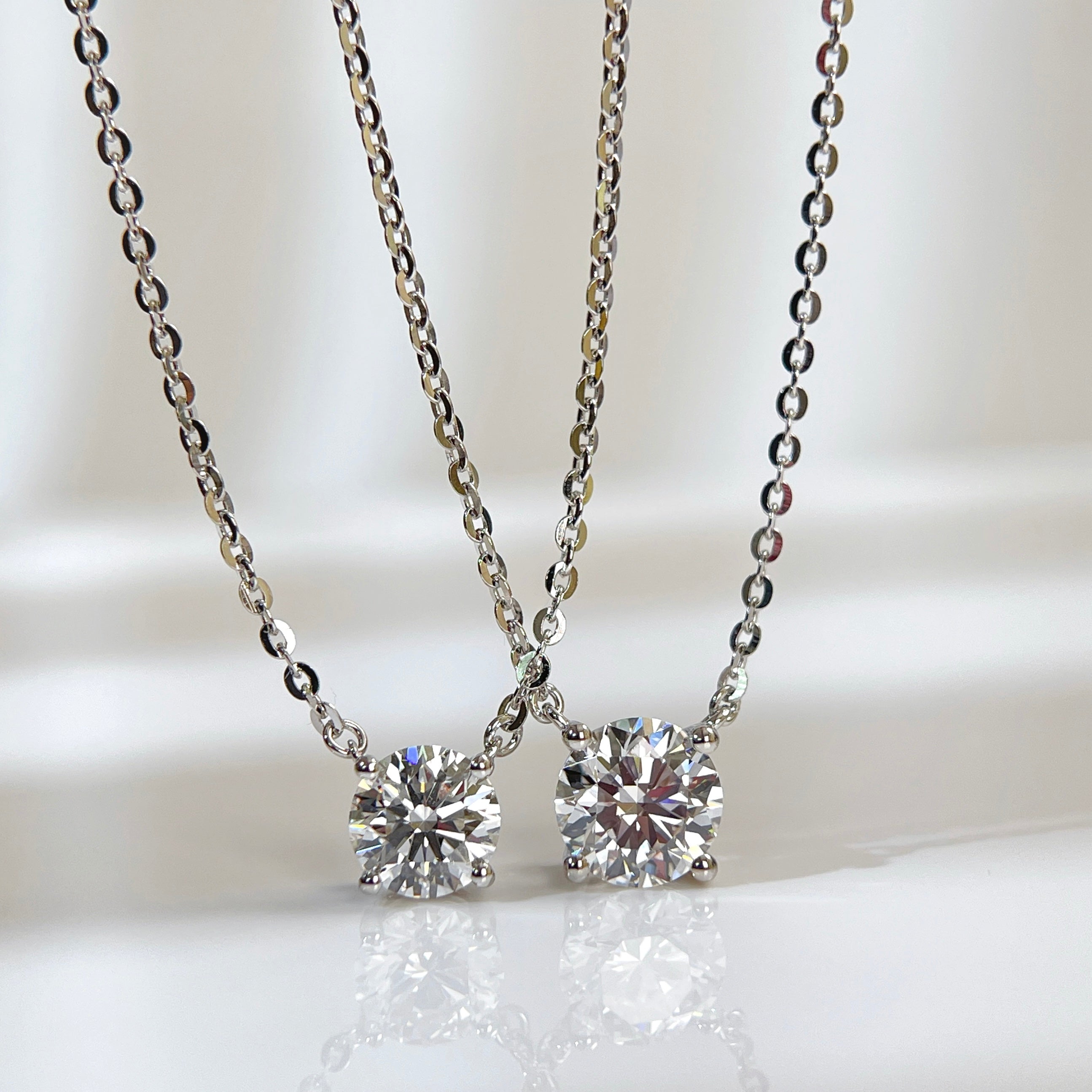 Jewelry display comparing 1 CT and 1.5 CT round lab grown diamond necklaces.
