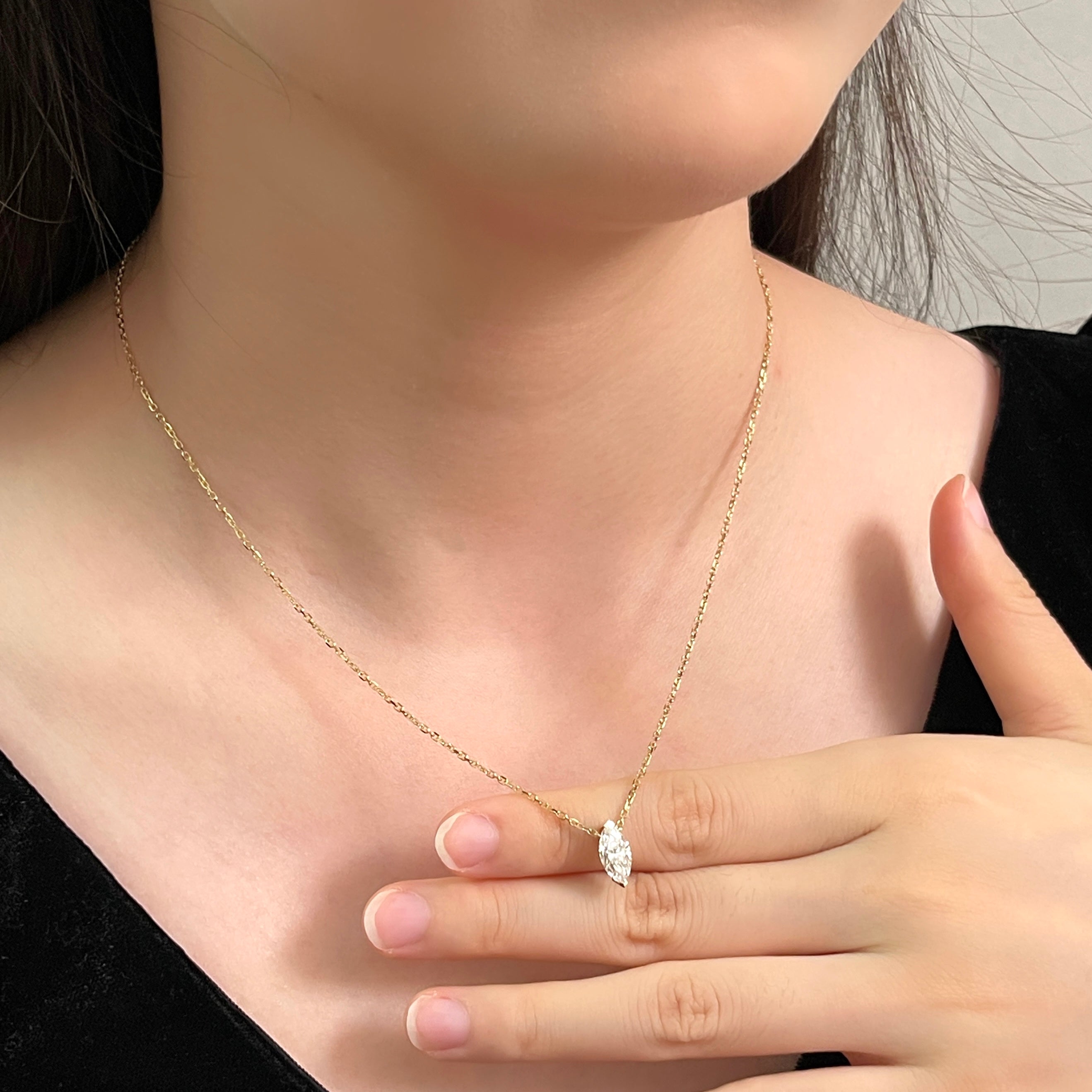 Model holding a 1 carat marquise lab grown diamond necklace in 18K yellow gold.