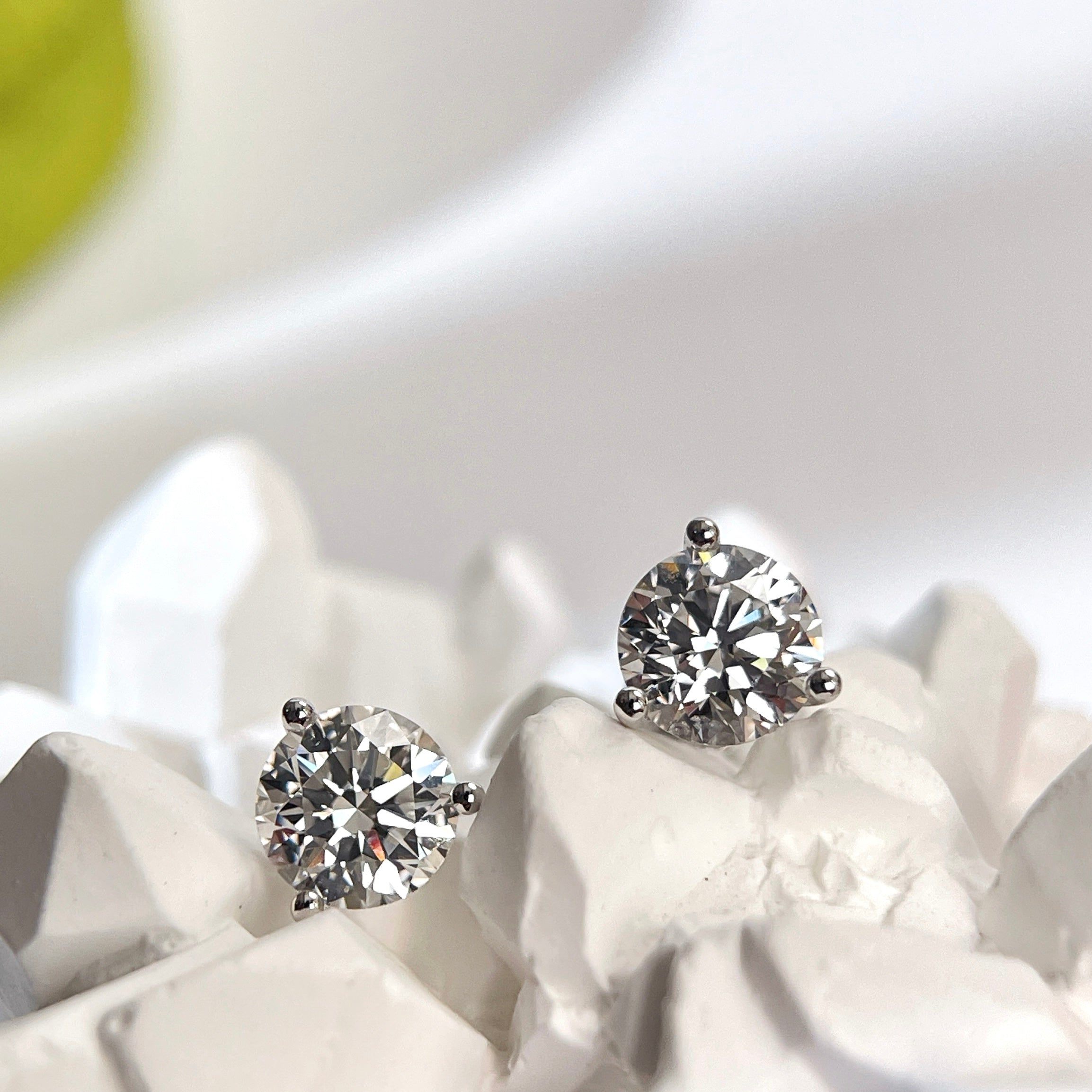 Round lab grown diamond Martini stud earrings displayed on a white sculptural background