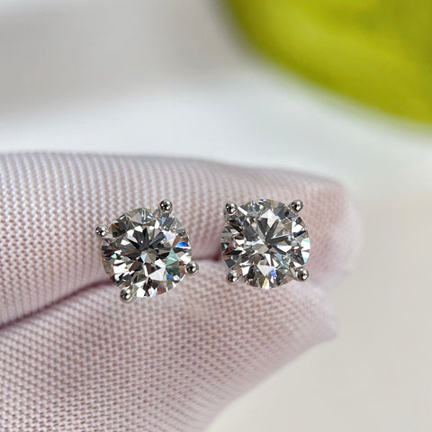 Gloved-hand close-up of D VVS2 round lab grown diamond four-prong stud earrings